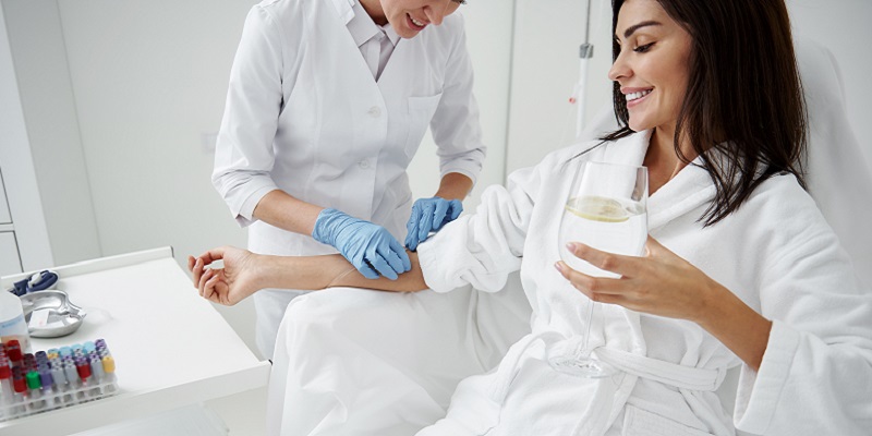 Doctor attaching intravenous drip on lady hand while she drinking water