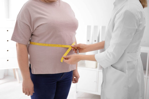 Doctor measuring waist of overweight woman in clinic, closeup
