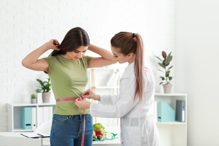 Doctor measuring waist of young woman in weight loss clinic