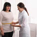 Nutritionist measuring overweight woman's waist with tape in clinic