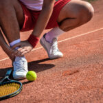 Sports injury. Close-up of tennis player touching his leg while sitting on the tennis court