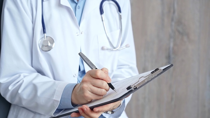 Healthcare professional doctor writing medical records on a clipboard. Female unrecognizable physician at work.