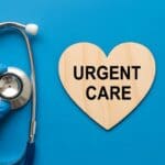 Doctors hand in blue glove holding stethoscope near wooden heart sign with urgent care