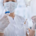 Nurse in protective mask and gloves preparing intravenous infusion drip for patient
