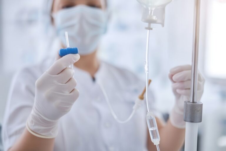 Nurse in protective mask and gloves preparing intravenous infusion drip for patient