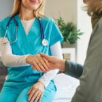 Cropped portrait of smiling woman nurse in medical uniform shaking hands with mature elderly female patient sitting on couch in office during examination in clinic.